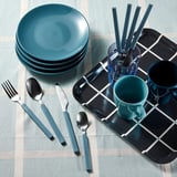 Apparecchiare la tavola con piatti, tazze e utensili verde acqua. Le posate includono forchetta, coltello, cucchiaio e cucchiaino, organizzati su un vassoio in bianco e nero.