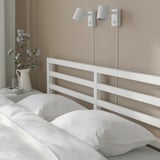 Un letto bianco ben fatto con cuscini e decorazioni floreali sul comodino, che mostra la funzionalità delle testate per la lettura.