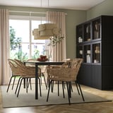 Sala da pranzo moderna con grande tappeto TIDTABELL, sedie in vimini, tavolo in vetro, scaffali scuri, pareti verde chiaro e grande finestra.