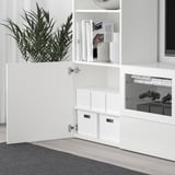 Viene mostrato un mobile contenitore TJENA bianco, con scomparti e cassetti aperti, che contiene controller di gioco.