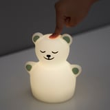 La mano del bambino interagisce con la luce notturna TÖVÄDER. La luce, a forma di orso, si illumina in più colori e regola automaticamente la luminosità.