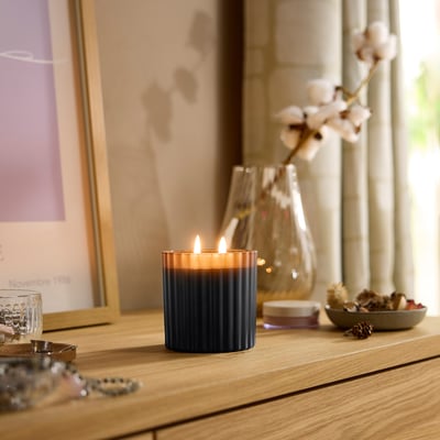 Interni accoglienti con candela blu TOFSTÄRNA accesa su uno scaffale di legno, circondato da oggetti decorativi.