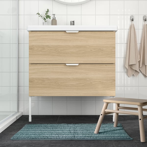 Bagno moderno con lavabo in legno, bancone bianco e tappetino TOFTBO blu.