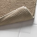 Tappetini da bagno beige impilati con strato antiscivolo in rete sottostante.