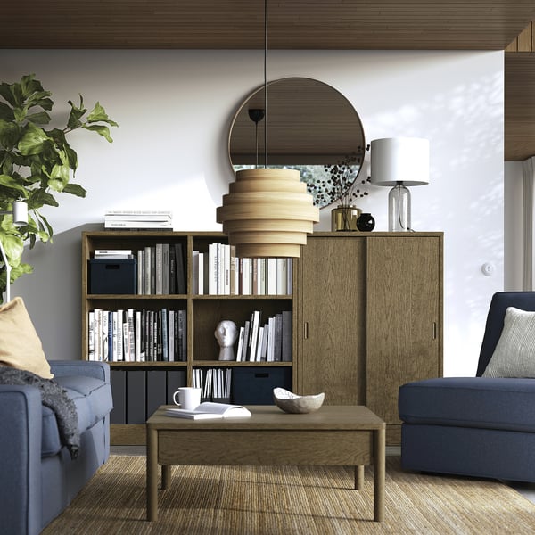 Soggiorno moderno con libreria TONSTAD, divani blu e specchio rotondo.