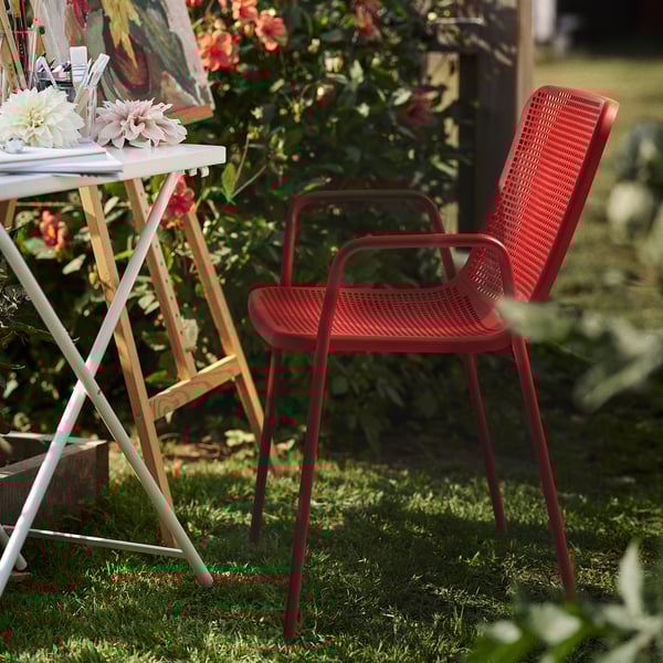 Sedia torparø rossa con seduta intrecciata in giardino accanto al tavolo con fiori.