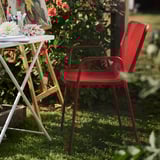 Sedia torparø rossa con seduta intrecciata in giardino accanto al tavolo con fiori.