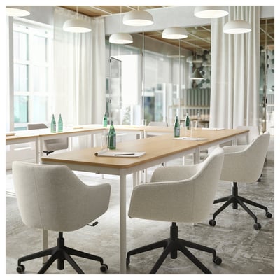 Moderno ufficio con lungo tavolo in legno, sedie imbottite bianche, bottiglie d'acqua verdi e lampade a sospensione.