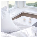 Camera da letto bianca con candele; Arredamento nitido e pulito. Candele accese sul davanzale della finestra, atmosfera morbida.