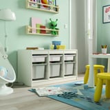Stanza dei giochi con mobile contenitore TROFAST, verde chiaro, legno, basso, cubi per riporre gli oggetti, vicino alle sedie gialle e porta aperta.