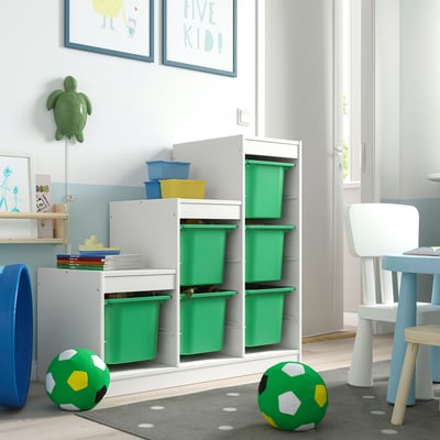 Unità TROFAST colorata: cornice bianca, bidoni verdi, accessori blu nella stanza dei giochi per bambini con decorazioni a tartaruga.
