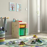 Area giochi per bambini con contenitore TROFAST in legno, bidoni verde brillante, giocattoli e tappeto colorato.