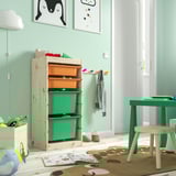 Camera per bambini con contenitore TROFAST, scatole colorate, struttura in legno. Mobili luminosi, decorazioni giocose, porta aperta e libri sul pavimento.