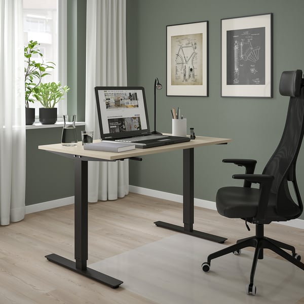 Scrivania regolabile TROTTEN in beige con laptop, libri e sedia. Due diagrammi di biciclette sono appesi sopra.