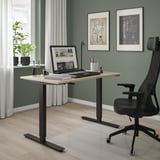 Scrivania regolabile TROTTEN in beige con laptop, libri e sedia. Due diagrammi di biciclette sono appesi sopra.