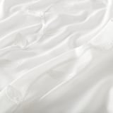 Tende bianche trasparenti con intricati motivi a foglie, finemente dettagliate, pendono elegantemente, offrendo uno scorcio di luce naturale e una sottile privacy.