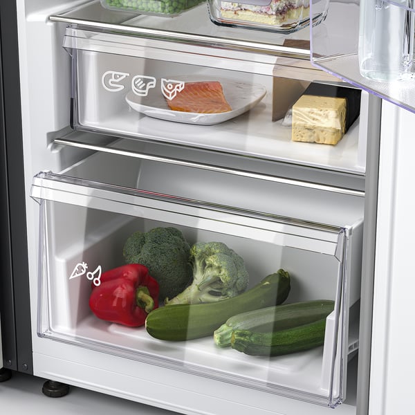 Frigo aperto con le verdure nel cassetto: broccoli, peperoni, zucchine, più pesce sul ripiano superiore.