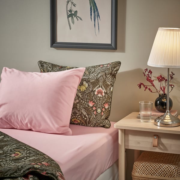 Letto con lenzuola rosa ULLVIDE, cuscino floreale, arte murale incorniciata, lampada, vetro sul comodino.