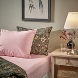 Letto con lenzuola rosa ULLVIDE, cuscino floreale, arte murale incorniciata, lampada, vetro sul comodino.