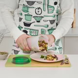Persona che tiene in mano lo shaker UPPFYLLD, versando l'insalata sciacquata su un piatto su una tavola di legno. Il grembiule utensili da cucina disegni.