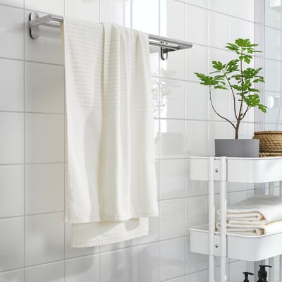 Asciugamani VÅGSJÖN bianchi su barra cromata in bagno minimalista con caddy.