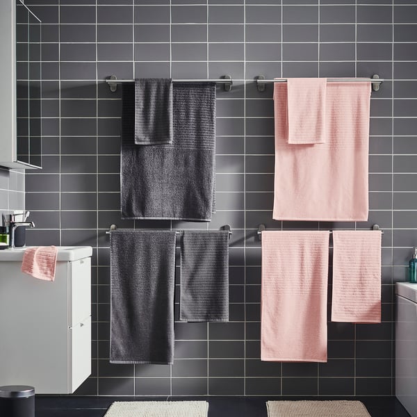 Bagno moderno con pareti piastrellate grigie e asciugamani appesi: tre neri, due rosa. Elegante e minimalista.