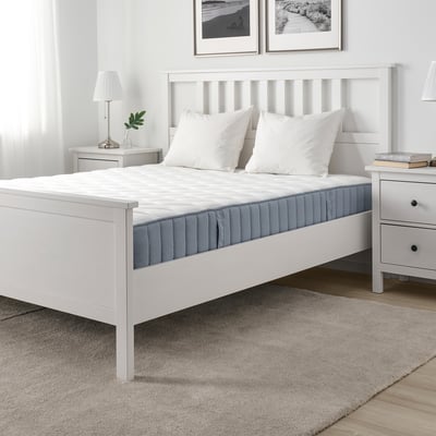 Camera da letto moderna con letto VÅGSTRANDA, materasso rigido, cuscini, tappeto grigio, comodini e opere d'arte alle pareti.