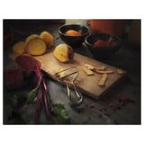 Tagliere in legno con pelapatate e verdure colorate: barbabietole rosse, radice gialla, foglie verdi. Spezie e pelapatate.