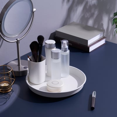Vanità per il trucco sul bancone blu, vassoio rotante con pennelli, bottiglie, compatto, rossetto e candela.