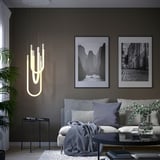 Soggiorno moderno con pareti scure, lampada VARMBLIXT, divano grigio, cuscini, coperta, arte del paesaggio, tavoli decorativi, pianta per finestra, design minimalista.