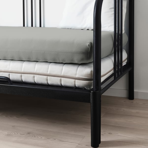 Struttura letto in metallo nero con lenzuola e materasso grigi.