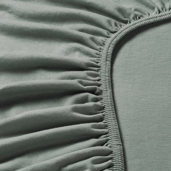 Primo piano del morbido tessuto jersey verde con bordo elastico, che mostra texture e cuciture di qualità.