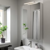 Bagno moderno con lampada VÅTHULT sopra il lavandino, lo specchio e la pianta.