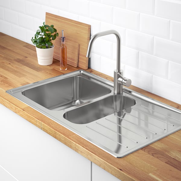 Lavello da cucina in acciaio inox con gocciolatoio e rubinetto su piano di lavoro in legno, accanto a una pianta.