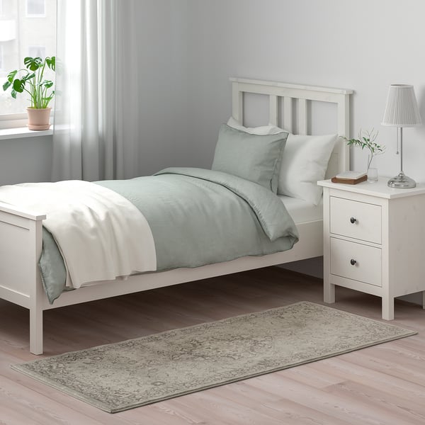 Camera da letto con tappeto floreale VEDBÄK grigio accanto al letto bianco, che si abbina alle tende grigio chiaro.