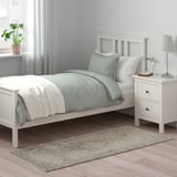Camera da letto con tappeto floreale VEDBÄK grigio accanto al letto bianco, che si abbina alle tende grigio chiaro.