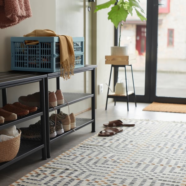 Cassa blu su scarpiera con coperta, pantofole, tappeto, sgabello, pianta; grande finestra.