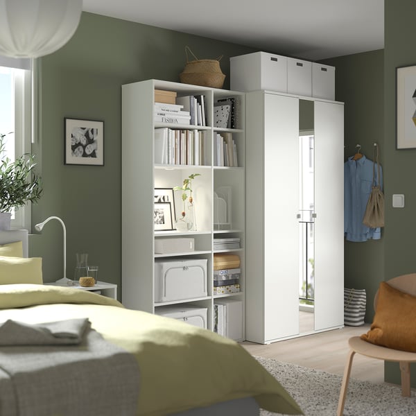 Camera da letto con pareti verdi, mobili bianchi: letto con coperta verde, scaffale e armadio con specchio.