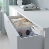 Cassettiera bianca con vestiti piegati. Tessuti grigio chiaro e beige ben organizzati. Design minimalista per camera da letto o soggiorno.