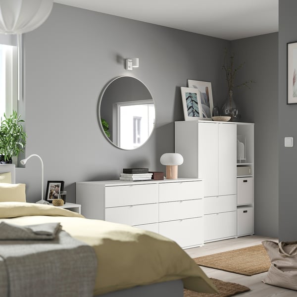 Camera da letto moderna con pareti grigie, mobili bianchi, coperta gialla, specchio rotondo, lampada e oggetti decorativi.