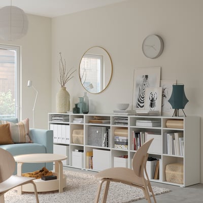 Soggiorno moderno con mensole VIHALS bianche, divano azzurro, sedia in legno e oggetti decorativi.