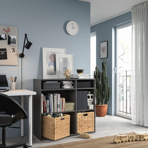 Moderno home office blu con mobile contenitore VIHALS grigio scuro, scrivania bianca, sedia nera, orologio da parete e grande finestra con tende bianche.