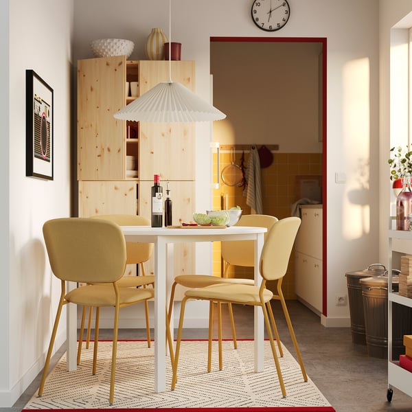 Quattro sedie VIHALS, beige, attorno a un tavolo bianco. Armadio in legno chiaro, arredamento colorato. Cucina moderna a vista.