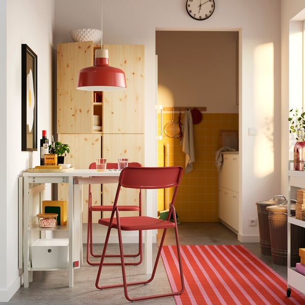 Soggiorno moderno con tavolo bianco a scomparsa, sedie rosse, cucina gialla sullo sfondo.