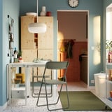 Zona pranzo compatta con tavolo allungabile, due sedie verdi, decorazione, tappeto verde, accenti blu, lampada a sospensione, porta della cucina.