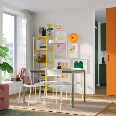 Allestimento da pranzo luminoso e moderno con tavolo VIHALS giallo, sedie bianche, accenti verdi e arte murale.