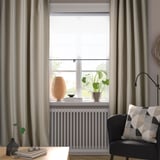 Camera accogliente con tende grigie VILBORG, sedia nera, pianta in stile, lampada e libri.