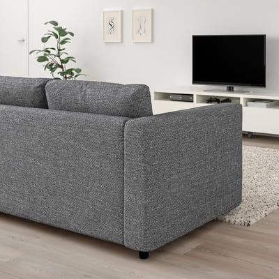 Soggiorno moderno con grande divano grigio VIMLE contro il muro, tv a schermo piatto su supporto, pianta e tappeto; Arredamento minimalista.