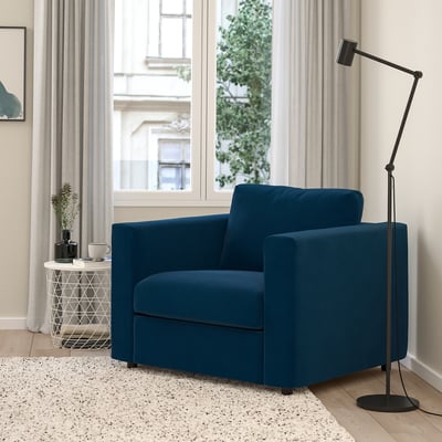 Soggiorno moderno con poltrona in velluto blu VIMLE, lampada e finestra con tende beige.