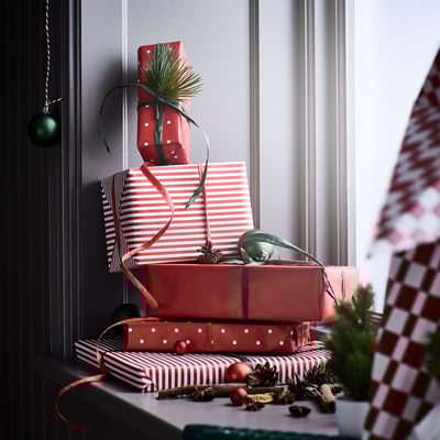 Regali di Natale impilati avvolti in carta rossa e bianca con nastro verde e contorno di pino.